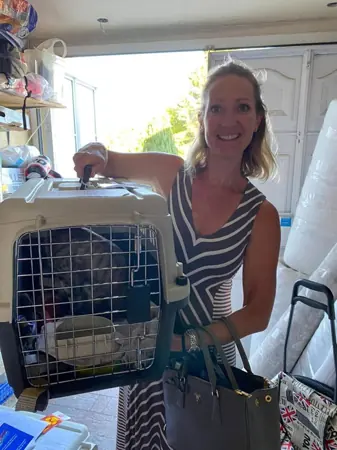 A smiling woman beside her cat’s travel carrier.