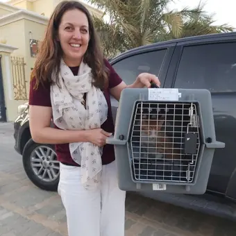 A woman outdoors beside her cat’s travel carrier.